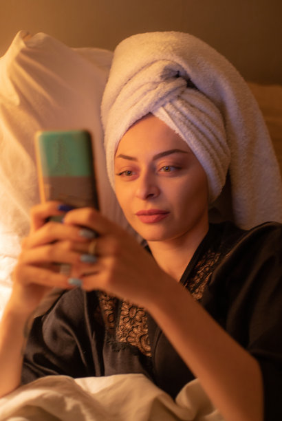 年轻美丽的女人坐在她的卧室准备睡觉，玩她的智能手机，发短信和上网。图片下载