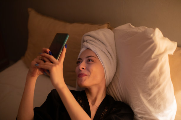 年轻美丽的女人坐在她的卧室准备睡觉，玩她的智能手机，发短信和上网。图片下载