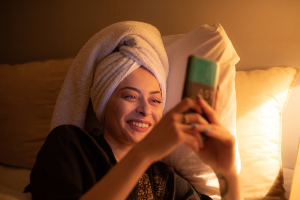 年轻美丽的女人坐在她的卧室准备睡觉，玩她的智能手机，发短信和上网。图片下载