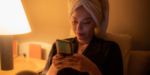 年轻美丽的女人坐在她的卧室准备睡觉，玩她的智能手机，发短信和上网。图片下载