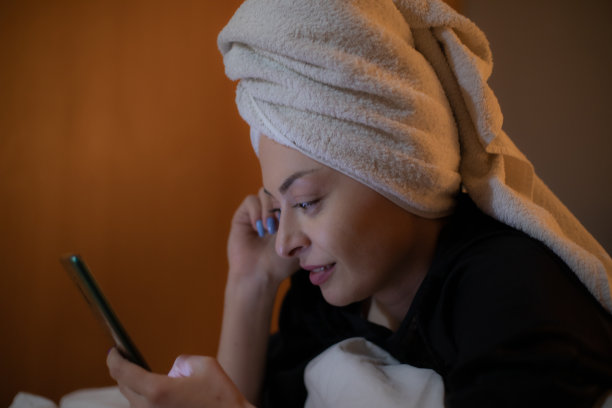 年轻美丽的女人坐在她的卧室里准备睡觉，玩她的智能手机，发短信和上网。图片下载