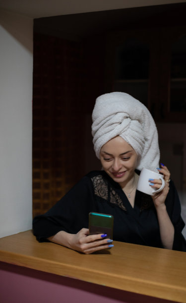 年轻美丽的女人坐在她的卧室准备睡觉，玩她的智能手机，发短信和上网。图片下载