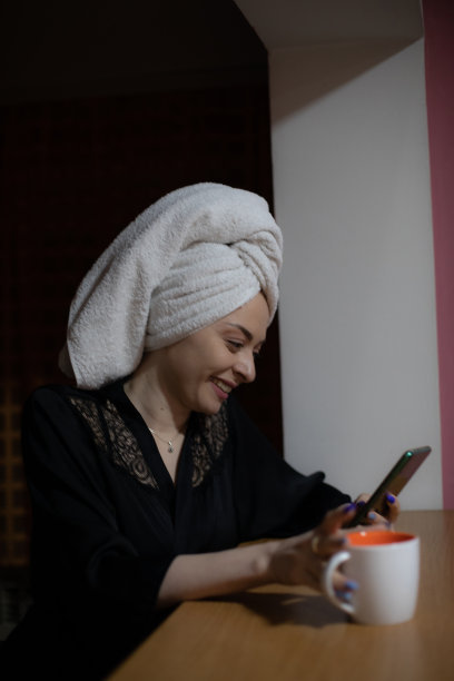 年轻美丽的女人坐在她的卧室准备睡觉，玩她的智能手机，发短信和上网。图片下载