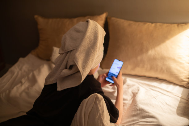 年轻美丽的女人坐在她的卧室准备睡觉，玩她的智能手机，发短信和上网。图片下载