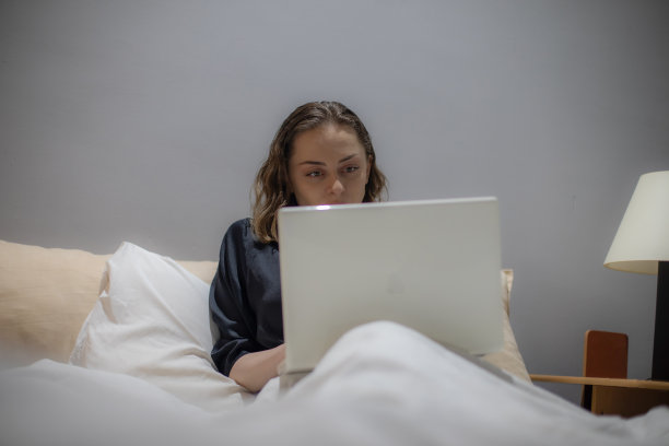 年轻美丽的女人坐在她的卧室准备睡觉，在她的笔记本电脑上工作，整理和准备第二天，休息和上网。图片下载