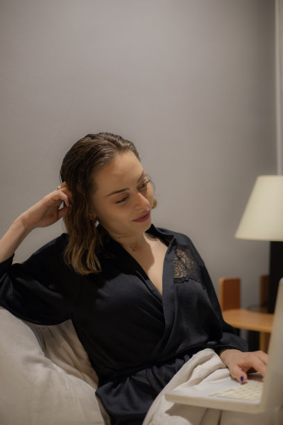 年轻美丽的女人坐在她的卧室准备睡觉，在她的笔记本电脑上工作，整理和准备第二天，休息和上网。图片下载