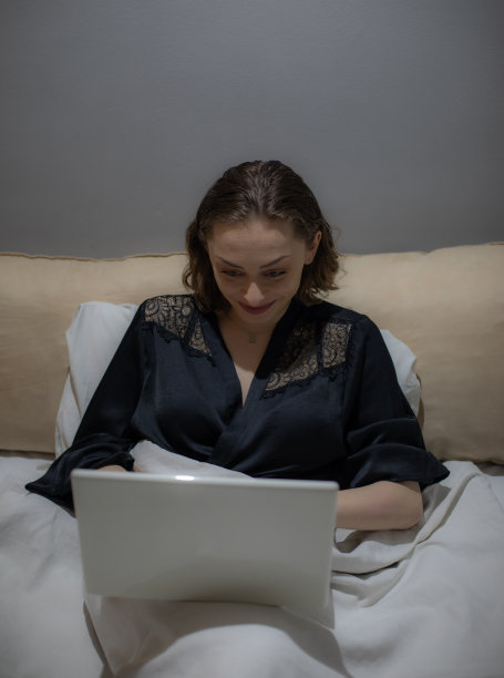 年轻美丽的女人坐在她的卧室准备睡觉，在她的笔记本电脑上工作，整理和准备第二天，休息和上网。图片下载