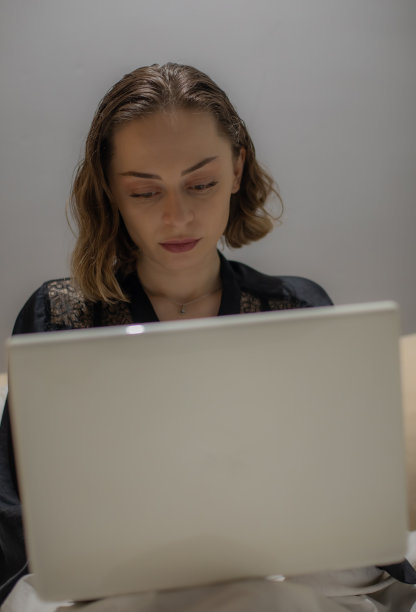 年轻美丽的女人坐在她的卧室准备睡觉，在她的笔记本电脑上工作，整理和准备第二天，休息和上网。图片下载