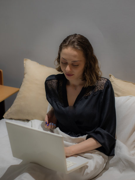 年轻美丽的女人坐在她的卧室准备睡觉，在她的笔记本电脑上工作，整理和准备第二天，休息和上网。图片下载