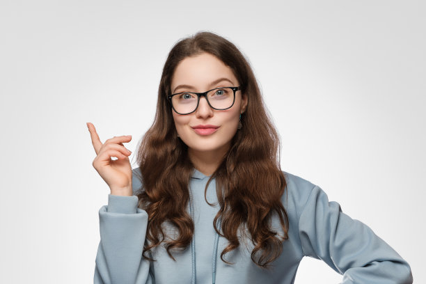 一个留着长发，戴着眼镜，面带微笑的少女。女孩穿着一件紫色的超大号运动衫，向上指着。图片下载