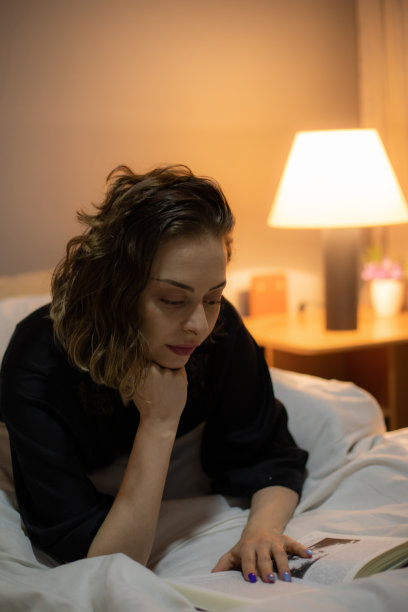 年轻美丽的女人坐在她的卧室里读一本书，她睡觉前，放松在她舒适的床上。图片下载