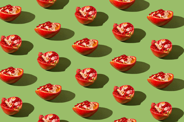 创意图案由半新鲜的石榴在绿色背景与阴影。点心的概念。健康食品配料主题。图片下载