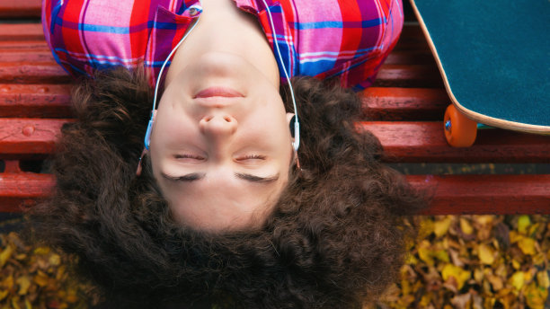 一个玩滑板的少女坐在长椅上听音乐。图片下载