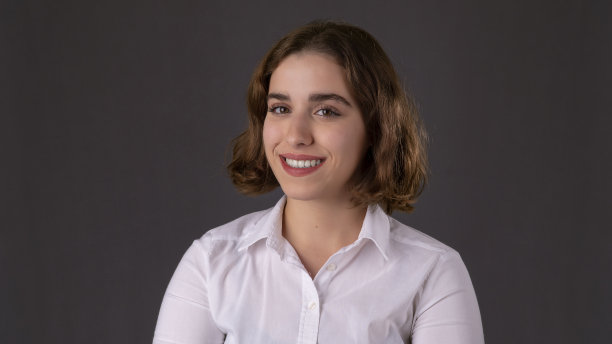 在灰色背景前穿着白衬衫微笑的女商人的肖像。可爱的短发女孩。她似乎对他工作上的成功感到高兴。她自豪地站着。图片下载