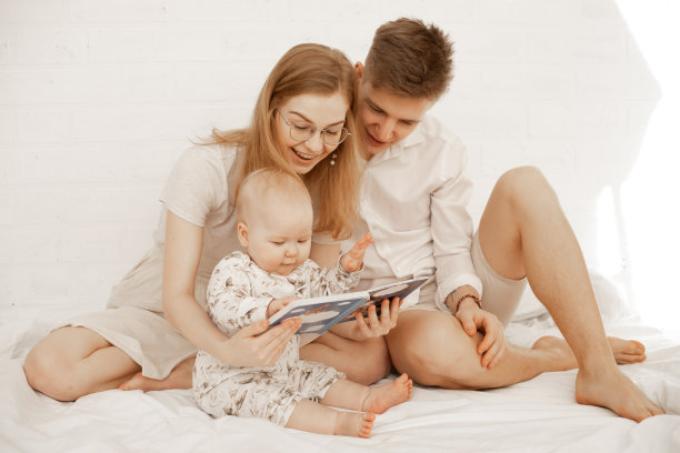 很高兴和家人在一起，光着脚的妈妈，爸爸，宝贝。阅读童话书，描述在亚麻卧室。图片下载
