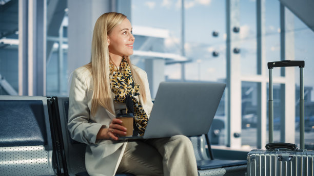机场候机楼:微笑的女子等待航班，使用笔记本电脑，浏览互联网，做电子商务，网上购物。旅行女性在航空枢纽的登机休息室用电脑在线远程工作图片下载