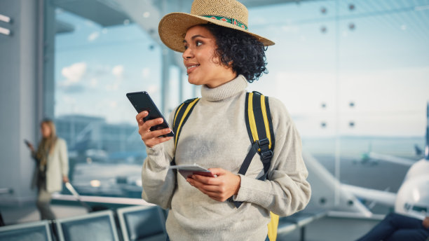 机场候机楼:快乐旅行的黑人女性在登机口等待登机，使用手机，在互联网上查看旅行目的地。微笑的非洲裔美国女性在度假图片下载