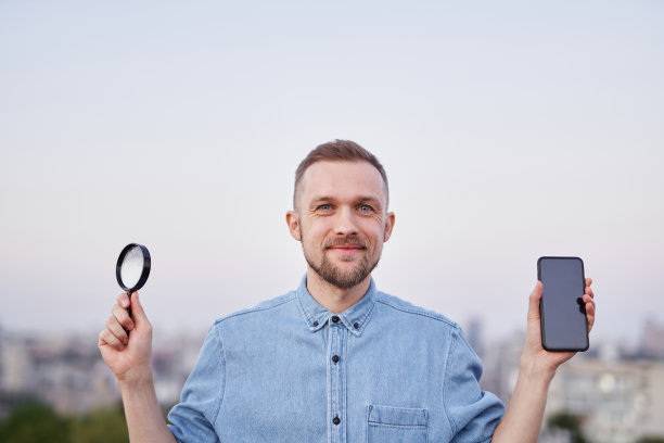 可爱快乐的男性拿着放大镜和智能手机看城市图片下载