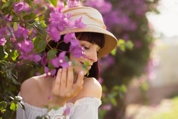 侧视图美丽的女孩穿着白色的连衣裙和草帽在盛开的樱花花园图片下载