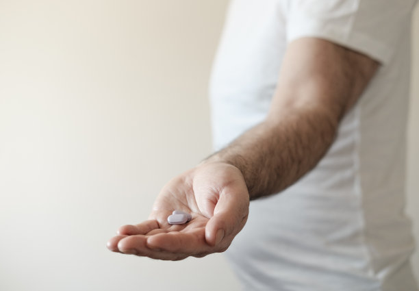 一个男人的手拿着一颗紫色的药丸。图片下载