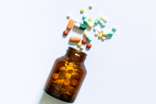 药丸和药瓶在白色背景上，药丸溢出到一个孤立的表面上的白色背景。图片下载