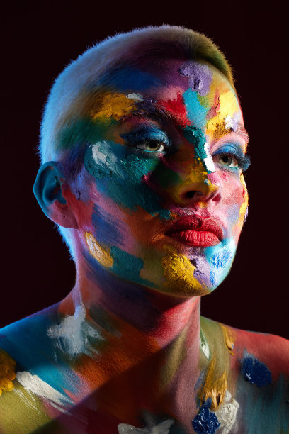 这是一名年轻女子脸上涂着彩色颜料摆姿势的画室照片图片下载