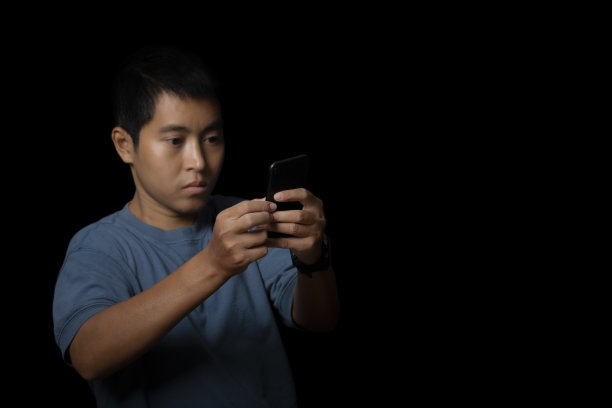 一个年轻人在黑色背景下使用智能手机的肖像。图片下载