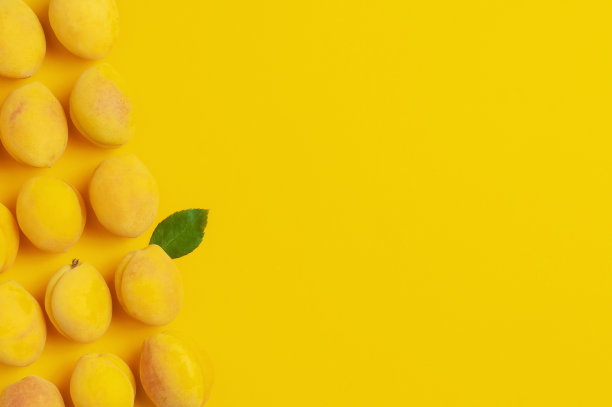 成熟新鲜的杏子果实，黄色背景的绿叶。平躺，顶视图，复制空间。新鲜的有机杏子，素食食品。创意杏模式。收获的概念图片下载