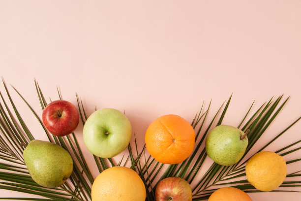 夏季热带布局由新鲜水果和绿色棕榈叶在一个柔和的粉红色背景。最小平。副本的空间。有机食物。图片下载