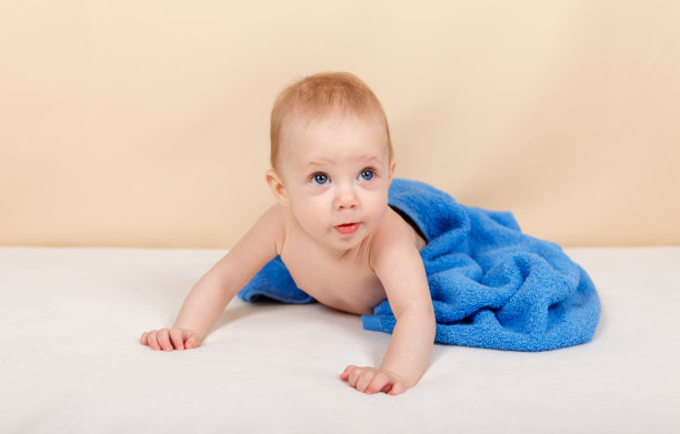 洗澡或淋浴后，穿着尿布和蓝色毛巾的男婴躺在床上图片下载