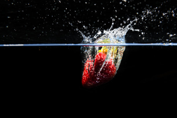 草莓落在水里，溅在黑色的背景上图片下载