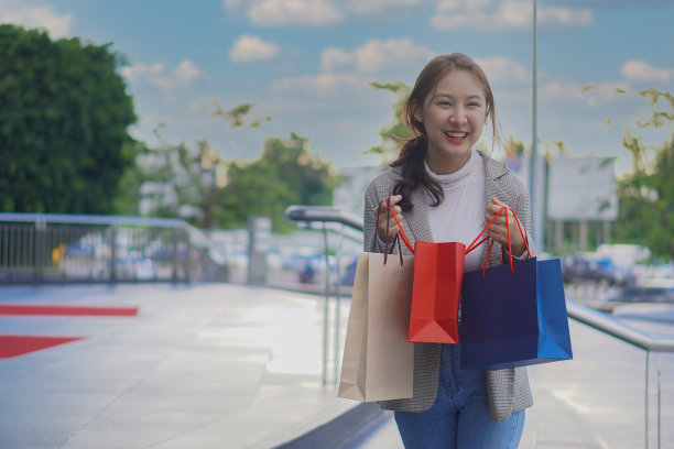 微笑的购物女孩在购物中心拿着五颜六色的购物袋站在购物中心模糊的背景图片下载