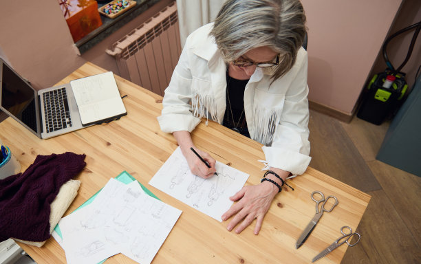 俯视图一个受启发的成熟的白人女性时装设计师服装设计师在她的创意设计师办公室或工作室画草图。年长时装、创造力。图片下载