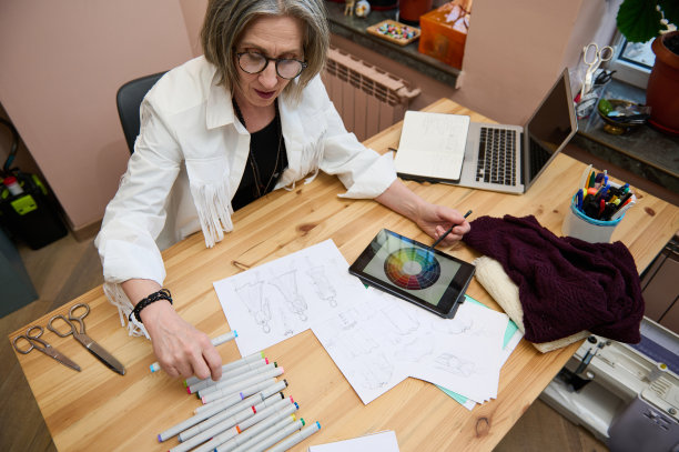成熟的白人女性裁缝服装设计师工作和画草图的衣服和选择颜色条在数字平板电脑。专业及职业:服装设计师。时尚的概念图片下载