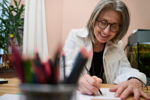 透过模糊的颜色笔筒看到快乐微笑的中年女性时装设计师在她的创意时装设计工作室创造新的服装线和服装收集灵感素描图片下载