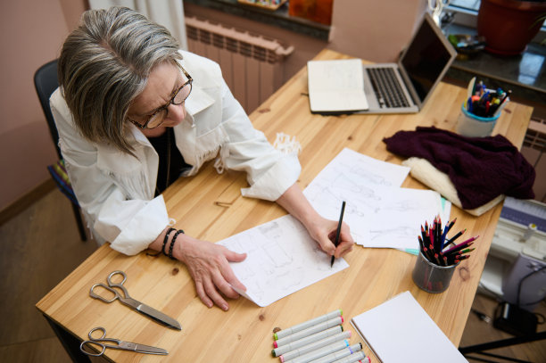 俯视图的中年女性时装设计师裁缝裁缝，老年女商人在她舒适的创意时装设计工作室为新的服装和服装系列绘制草图图片下载