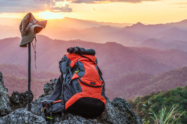 望远镜，帽子，日落时在岩石山顶上的背包。徒步露营和徒步探险的概念。图片下载