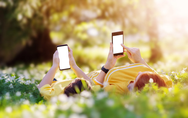 母亲和儿子拿着手机躺在公园的草地上图片下载