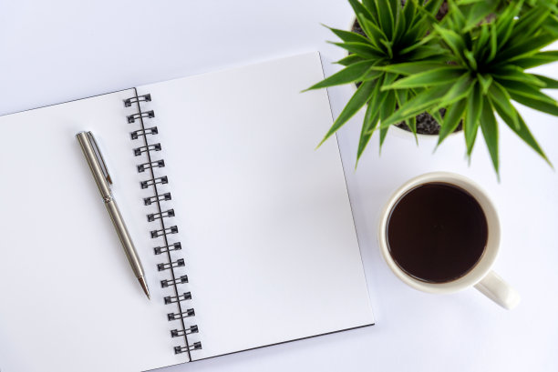 空白笔记本与咖啡，钢笔和绿色植物装饰在白色的桌子背景。图片下载