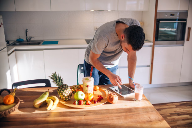 20多岁的素食主义者早上一边看平板电脑上的食谱，一边准备奶昔。图片下载