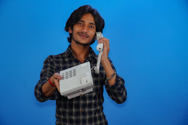 一个英俊的年轻人正在用蓝色背景的电话交谈图片下载