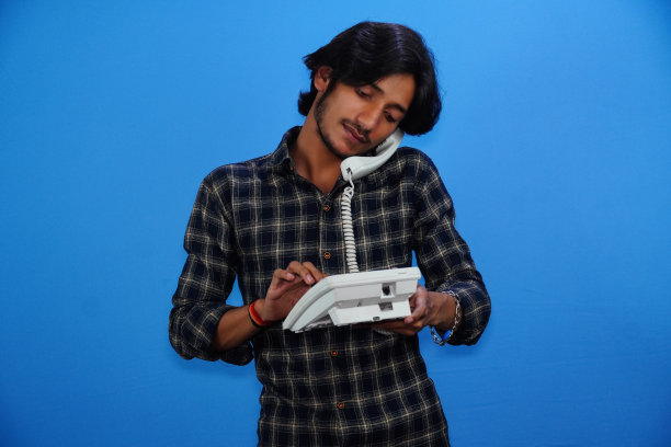 一个英俊的年轻人正在用蓝色背景的电话交谈图片下载