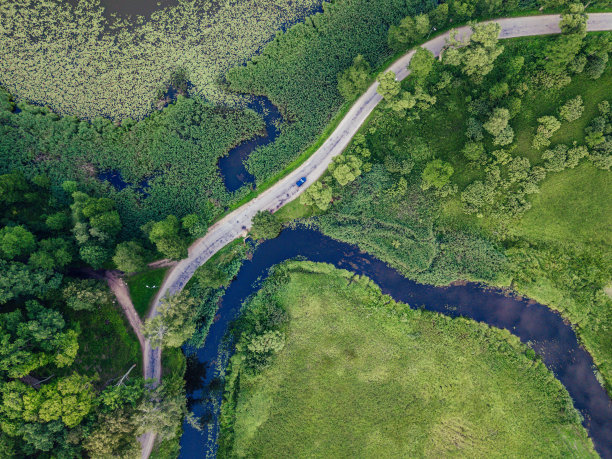 汽车在公路上行驶的航拍照片，在树下的河边，在早春阳光明媚的日子里俯瞰图片下载
