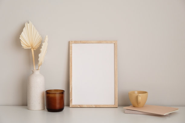 北欧风格的家庭办公办公桌在客厅。画框模型，蜡烛，花瓶里的干花，一杯茶，白色桌子上的纸笔记本。图片下载