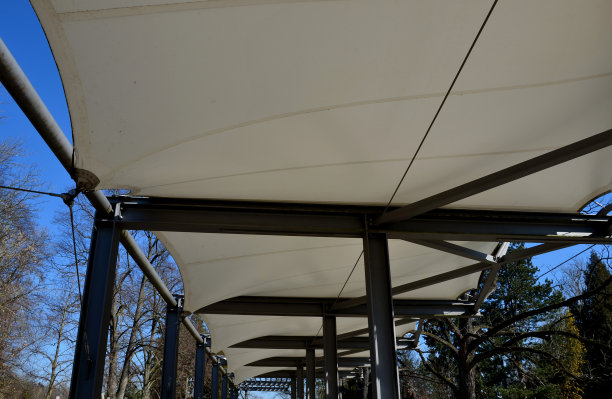 白色的帆布伸展开来，遮挡着阳光和雨水，覆盖在餐厅的露台上，幼儿园的操场上，在人行道的平台上。带有金属灰色横梁的藤架，用于攀爬植物图片下载