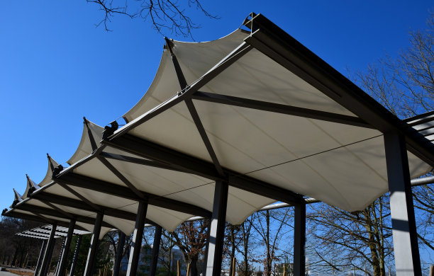 白色的帆布伸展开来，遮挡着阳光和雨水，覆盖在餐厅的露台上，幼儿园的操场上，在人行道的平台上。带有金属灰色横梁的藤架，用于攀爬植物图片下载