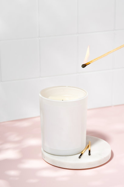 用一根火柴点燃一根由大豆蜡制成的芳香蜡烛。粉色桌子上的生态和素食蜡烛。芳香疗法芳香,放松。白色陶瓷背景上的极简主义概念图片下载