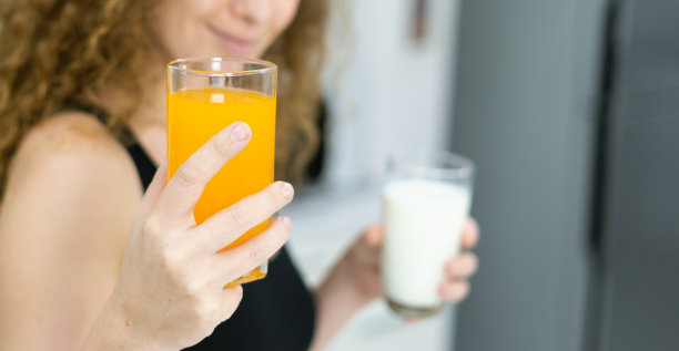 健康女性在厨房里一手拿橙汁杯，一手拿牛奶杯。美丽的白人妇女烹饪健康饮食水果或蔬菜在厨房图片下载