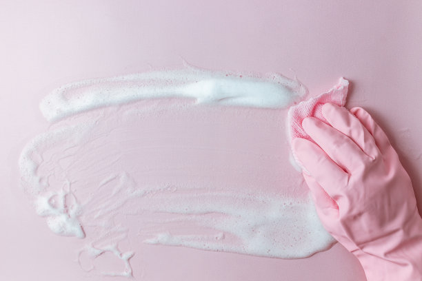 一只手戴着粉色橡胶手套，拿着清洁海绵，在粉红色的背景上擦肥皂泡沫。图片下载