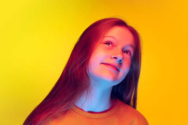 美丽的少女与梦幻表情摆姿势的特写肖像在霓虹灯黄色工作室背景孤立图片下载